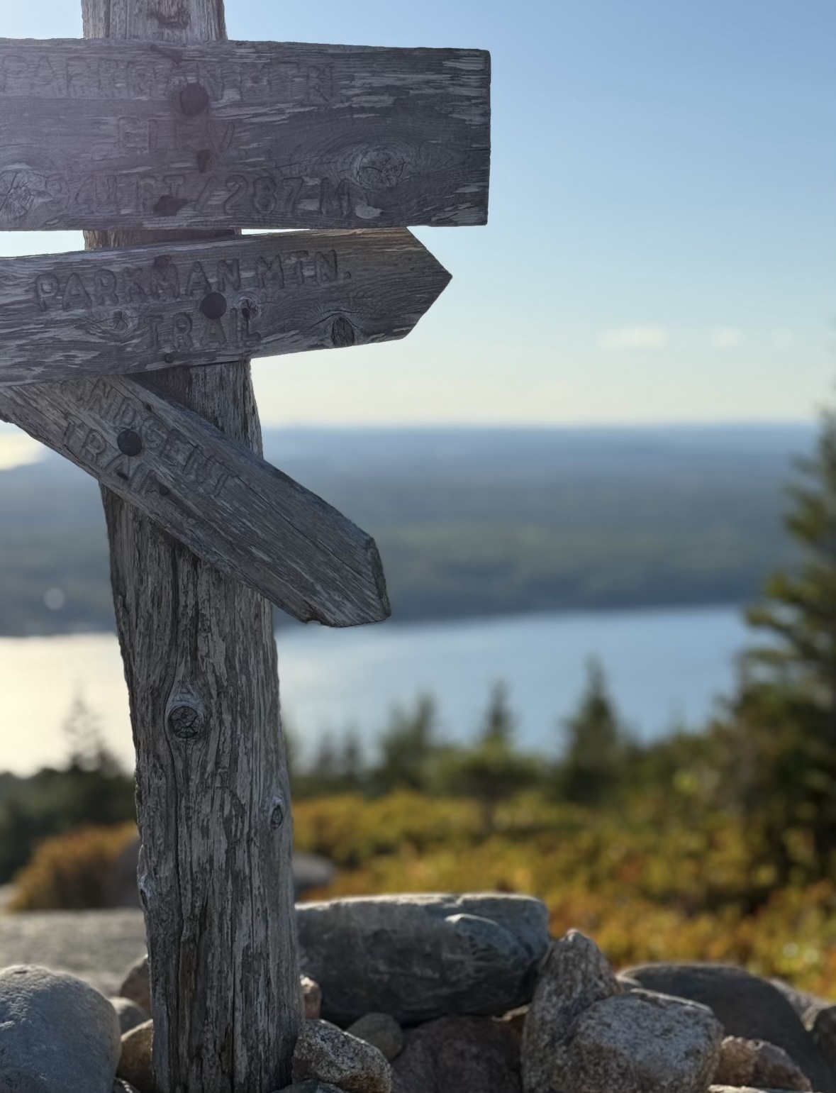 An old wooden trail sign on a mountaintop above a lake